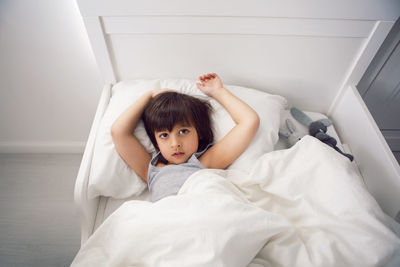 Child boy lies in a white children's bed with a blanket in a room with toys rabbits