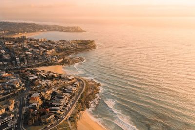 Aerial view of city by sea against sky during sunset