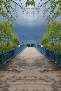 Footbridge along plants and trees against sky