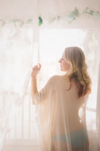 Woman looking away while standing against window