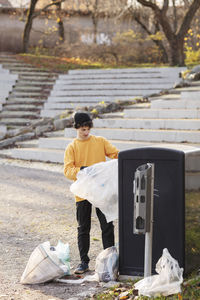 Male volunteer with plastic waste standing by garbage can