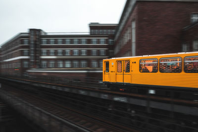 Yellow train on railway bridge in city against sky