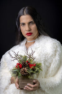 Portrait of young woman holding christmas flower bouquet against black background