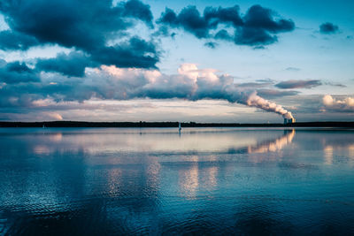 Wide shot of lake with sailboat and a coal power plant with fumes