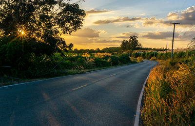 Road by trees against sky during sunset