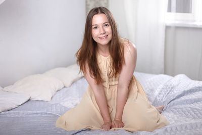 Portrait of smiling young woman sitting on bed at home