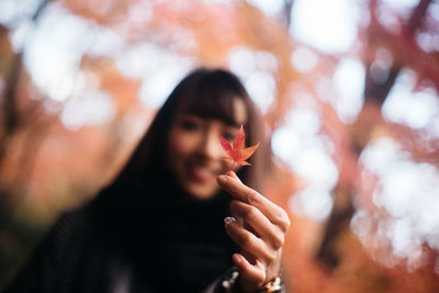 Close-up portrait of young woman holding maple leaf at park