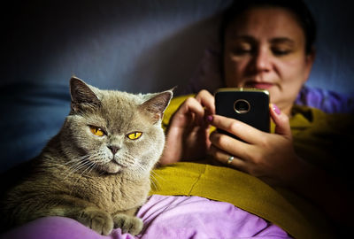 Portrait of cat sitting by mature woman using mobile phone on bed at home