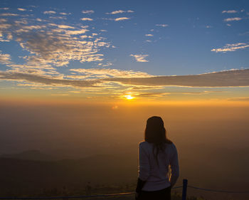 Rear view of woman standing against sky during sunset