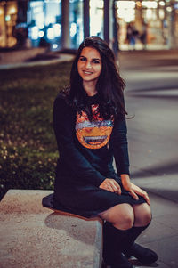 Portrait of smiling young woman sitting on street at night