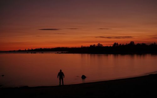 Silhouette man standing by lake against sky during sunset