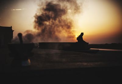 Silhouette person sitting against orange sky