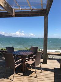 Empty chairs and table by sea against sky