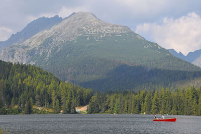 Couple in boat at lake by mountains against cloudy sky