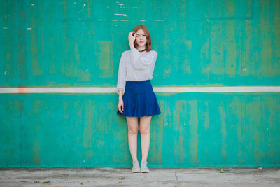 Full length portrait of young woman standing against blue wall