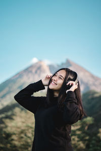 Smiling woman listening music against clear sky