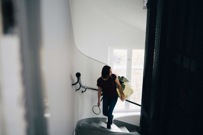 High angle view of woman carrying bag and badminton racket while climbing steps in new house