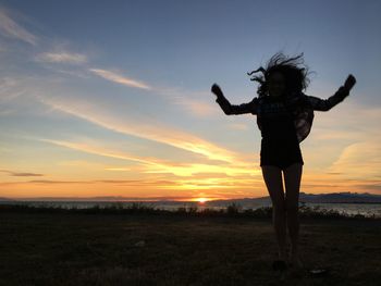 Full length of silhouette woman standing on field against sky during sunset