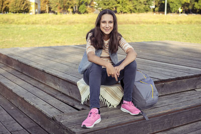 Portrait of a teenage girl student with a backpack sitting in a university park on an autumn day