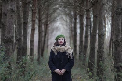 Young woman standing by tree trunk in forest during winter