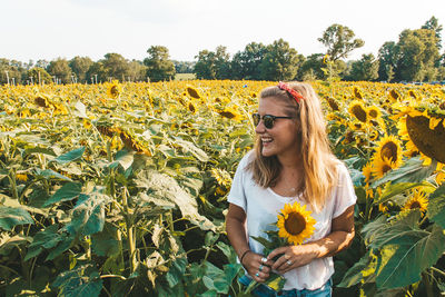 Happy beautiful young woman standing at sunflower field