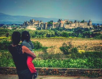 Rear view of woman standing on field against buildings