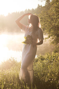 Side view of woman with arms raised standing on field