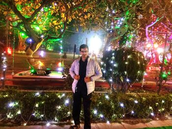 Portrait of man standing in illuminated christmas tree at night