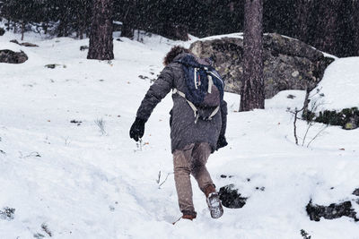 Rear view of man with backpack walking on snow covered field in forest