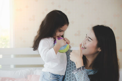 Mother gesturing with daughter holding ball at home