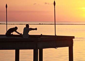 Man and woman exercising on pier against sea and sky during sunrise