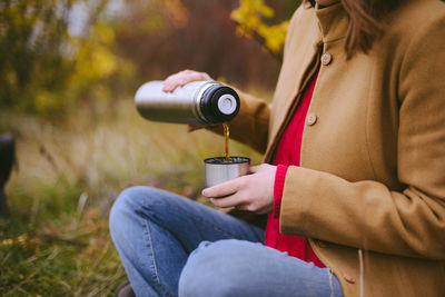 Midsection of woman pouring tea in cup on field