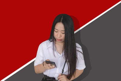 Young woman using smart phone against red background