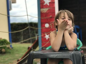 Girl looking away while sitting on chair at backyard