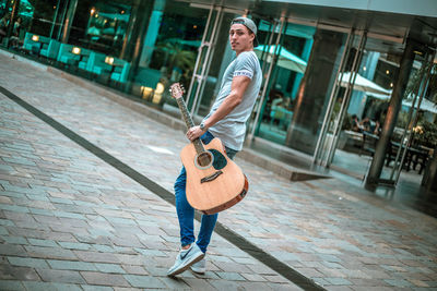 Full length of man playing guitar on footpath