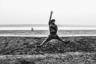 Full length of man with hand raised jumping at beach against sky