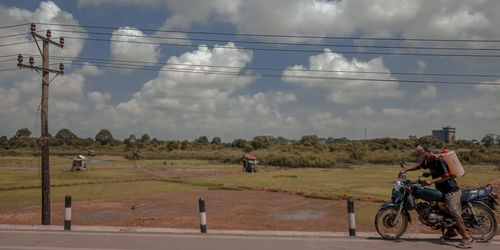 People riding motorcycle on field against sky