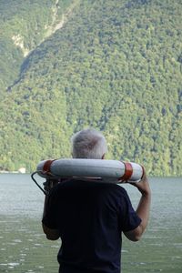 Rear view of man holding life belt by lake against mountain