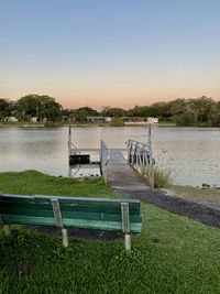 Empty bench by lake against clear sky