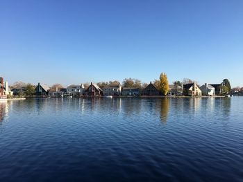 Houses by river against clear blue sky