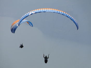 Low angle view of people paragliding against sky