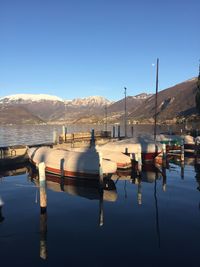 Boats moored in calm lake against clear blue sky