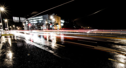 Light trails on wet street against sky at night