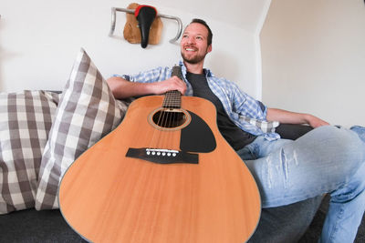 Smiling man with guitar sitting on sofa at home