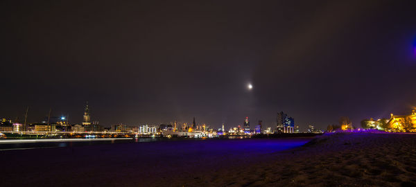 Illuminated cityscape by sea against sky at night