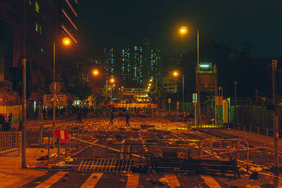 Illuminated street amidst buildings against sky at night