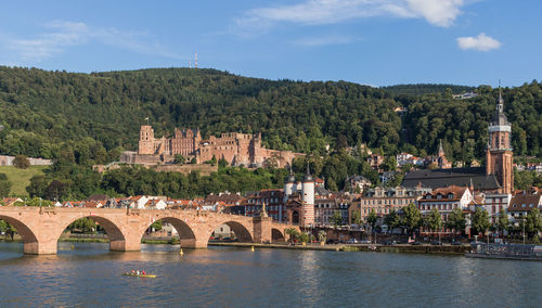 Arch bridge over river by buildings against sky