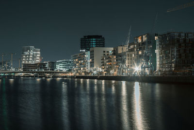 Illuminated buildings by sea against sky at night