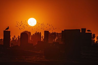 Silhouette buildings against orange sky during sunset