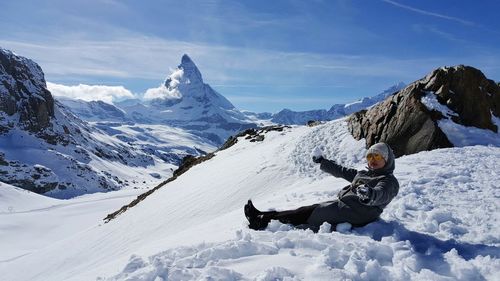 Full length of woman sitting on snowcapped mountain against sky